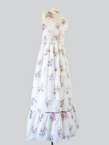 1970s white lace maxi dress with matching cropped jacket, featuring an allover lilac watercolor floral print, sweetheart neckline with scalloped lace trim, wide straps, lavender ribbon details, and a full flowing skirt. Fully lined two-piece vintage set