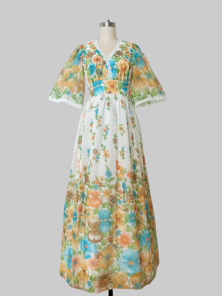 A 1970s vintage white maxi dress with a colorful floral print in orange, blue, and green.