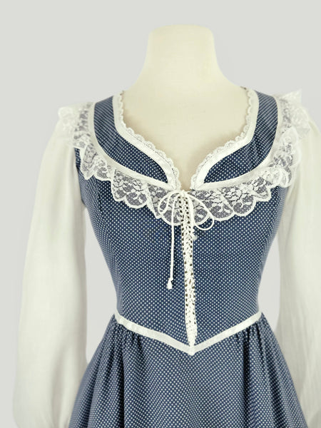 1970s Gunne Sax prairie dress in blue cotton with tiny white dots. Lace trimmed neckline with front tie, sheer white long sleeves, fitted waist and tiered ruffle hem