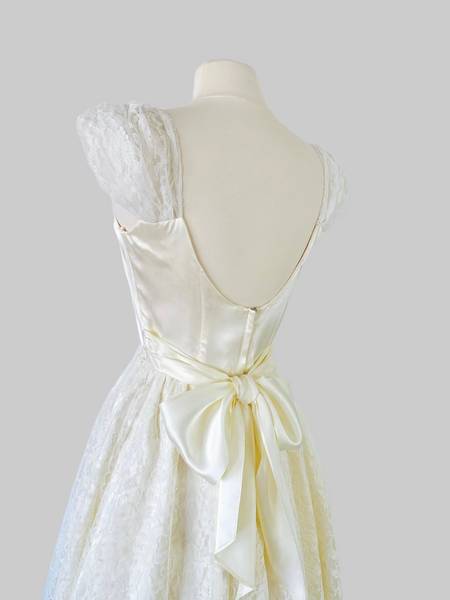 1980s ivory Gunne Sax bridal gown with a sleek satin bodice, graceful open back, and full-length layered skirt of floral lace, satin, and crinoline, finished with a satin waist tie.