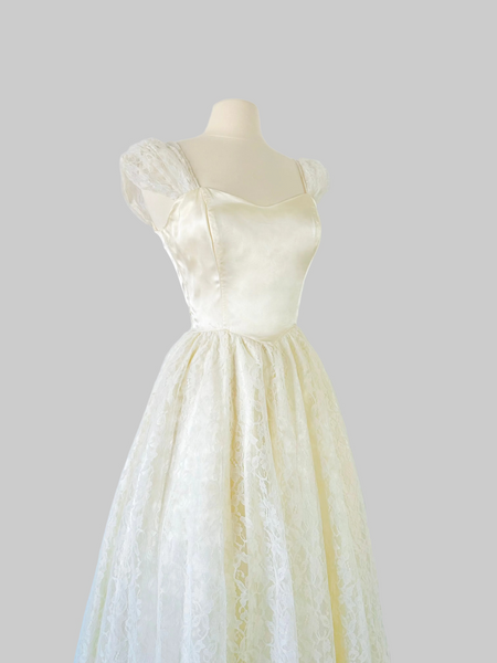 1980s ivory Gunne Sax bridal gown with a sleek satin bodice, graceful open back, and full-length layered skirt of floral lace, satin, and crinoline, finished with a satin waist tie.