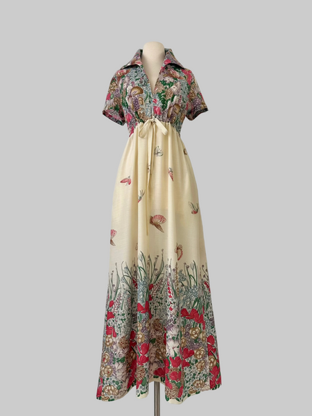 Vintage 1970s maxi dress featuring a floral and butterfly print, short sleeves, and a softly draped, full-length skirt.