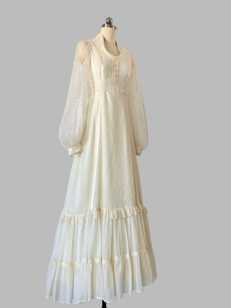 Vintage 1970s Gunne Sax gown in a soft candlelight hue, featuring a lace-adorned bodice with faux-pearl buttons, sheer patterned lace sleeves, and a tiered lace-trimmed skirt.