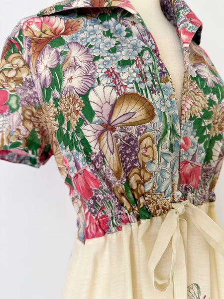 Vintage 1970s maxi dress featuring a floral and butterfly print, short sleeves, and a softly draped, full-length skirt.