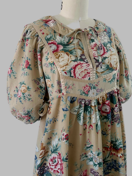 1970s honey-beige cotton midi dress by Plain Jane by Danuta featuring ribbon trim, puffed sleeves, empire waist with side ties, and a softly gathered flared skirt.