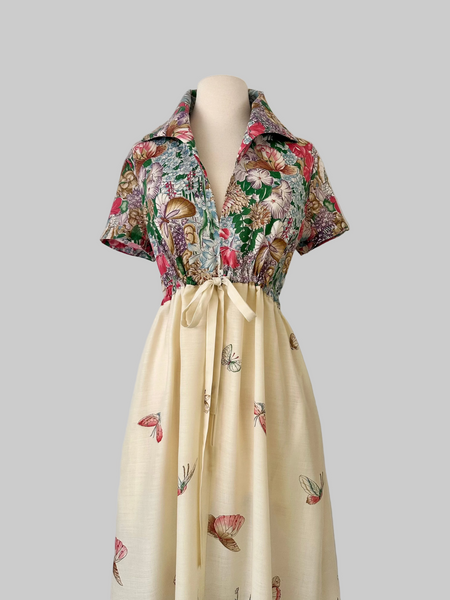 Vintage 1970s maxi dress featuring a floral and butterfly print, short sleeves, and a softly draped, full-length skirt.