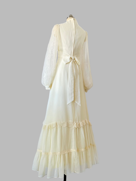 Vintage 1970s Gunne Sax gown in a soft candlelight hue, featuring a lace-adorned bodice with faux-pearl buttons, sheer patterned lace sleeves, and a tiered lace-trimmed skirt.