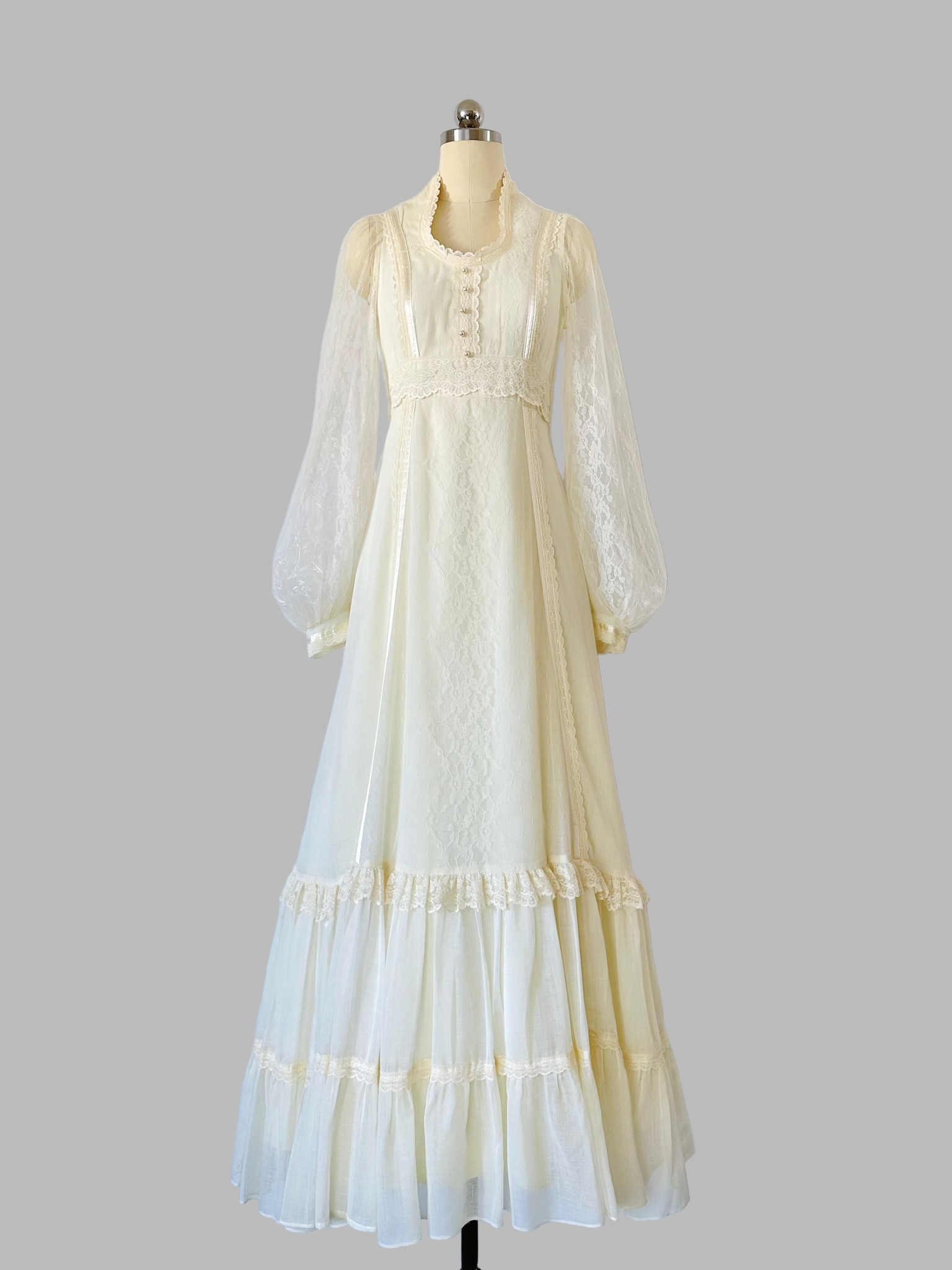 Vintage 1970s Gunne Sax gown in a soft candlelight hue, featuring a lace-adorned bodice with faux-pearl buttons, sheer patterned lace sleeves, and a tiered lace-trimmed skirt.