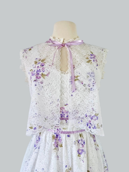 1970s white lace maxi dress with matching cropped jacket, featuring an allover lilac watercolor floral print, sweetheart neckline with scalloped lace trim, wide straps, lavender ribbon details, and a full flowing skirt. Fully lined two-piece vintage set