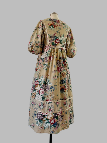 Back View of 1970s honey-beige cotton midi dress by Plain Jane by Danuta featuring ribbon trim, puffed sleeves, empire waist with side ties, and a softly gathered flared skirt.