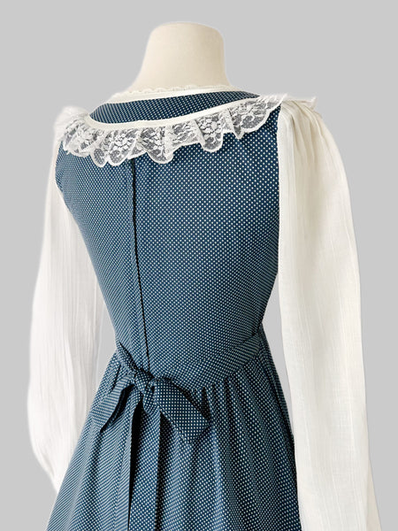 1970s Gunne Sax prairie dress in blue cotton with tiny white dots. Lace trimmed neckline with front tie, sheer white long sleeves, fitted waist and tiered ruffle hem