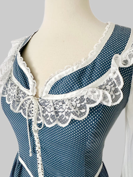 1970s Gunne Sax prairie dress in blue cotton with tiny white dots. Lace trimmed neckline with front tie, sheer white long sleeves, fitted waist and tiered ruffle hem