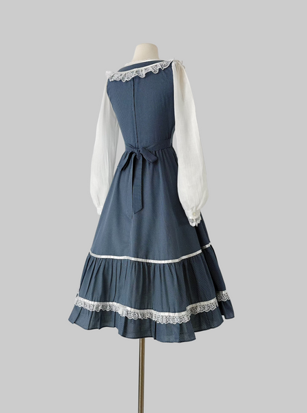 1970s Gunne Sax prairie dress in blue cotton with tiny white dots. Lace trimmed neckline with front tie, sheer white long sleeves, fitted waist and tiered ruffle hen
