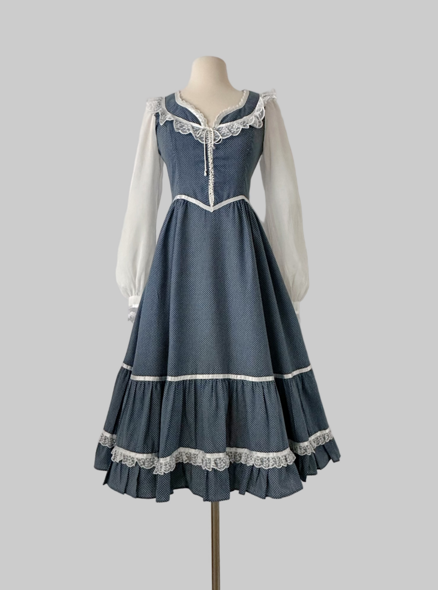 1970s Gunne Sax prairie dress in blue cotton with tiny white dots. Lace trimmed neckline with front tie, sheer white long sleeves, fitted waist and tiered ruffle hem