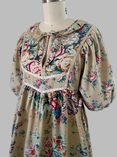 1970s honey-beige cotton midi dress by Plain Jane by Danuta featuring ribbon trim, puffed sleeves, empire waist with side ties, and a softly gathered flared skirt.