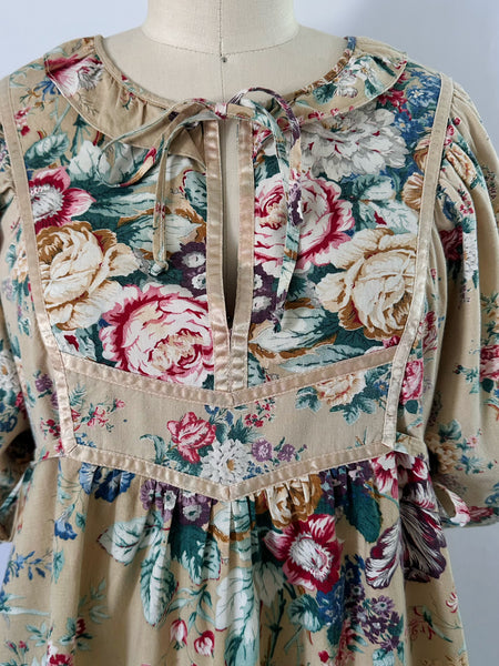 1970s honey-beige cotton midi dress by Plain Jane by Danuta featuring ribbon trim, puffed sleeves, empire waist with side ties, and a softly gathered flared skirt.