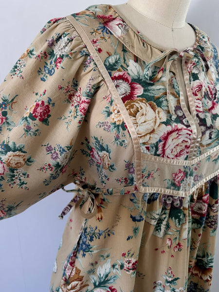 1970s honey-beige cotton midi dress by Plain Jane by Danuta featuring ribbon trim, puffed sleeves, empire waist with side ties, and a softly gathered flared skirt.