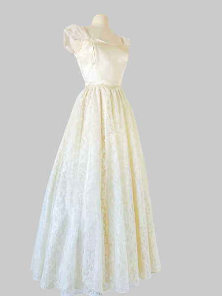 1980s ivory Gunne Sax bridal gown with a sleek satin bodice, graceful open back, and full-length layered skirt of floral lace, satin, and crinoline, finished with a satin waist tie.