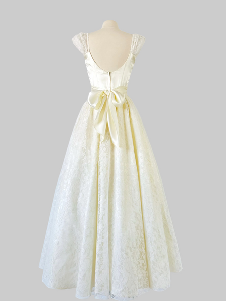 1980s ivory Gunne Sax bridal gown with a sleek satin bodice, graceful open back, and full-length layered skirt of floral lace, satin, and crinoline, finished with a satin waist tie.